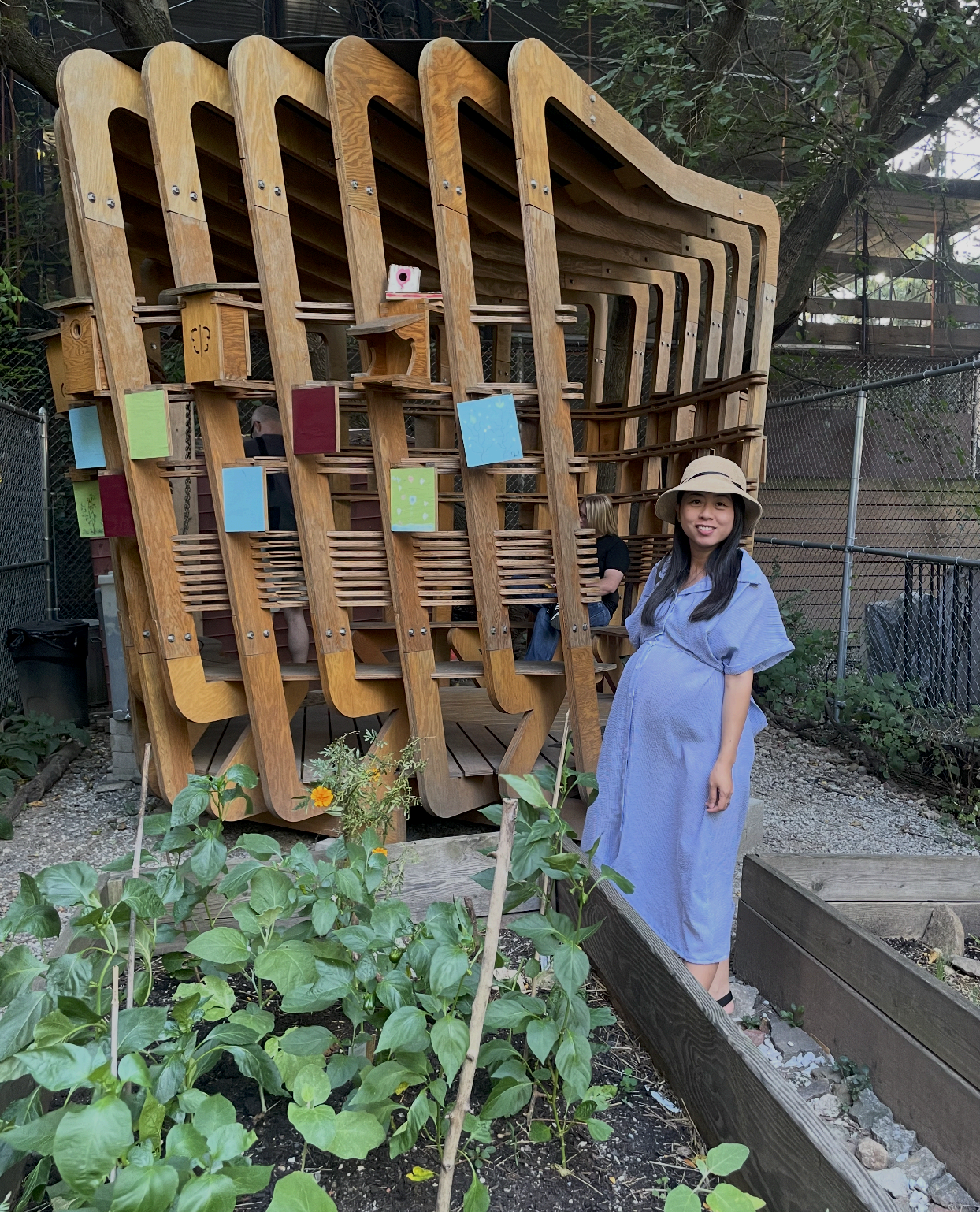 Cherry pregnant, wearing a blue dress and sun hat, standing in a community garden.
