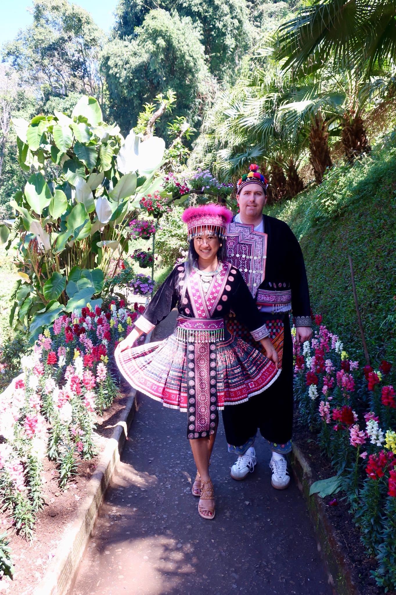 Brian and his wife wearing traditional Hmong dress in a colorful flower garden in northern Thailand.
