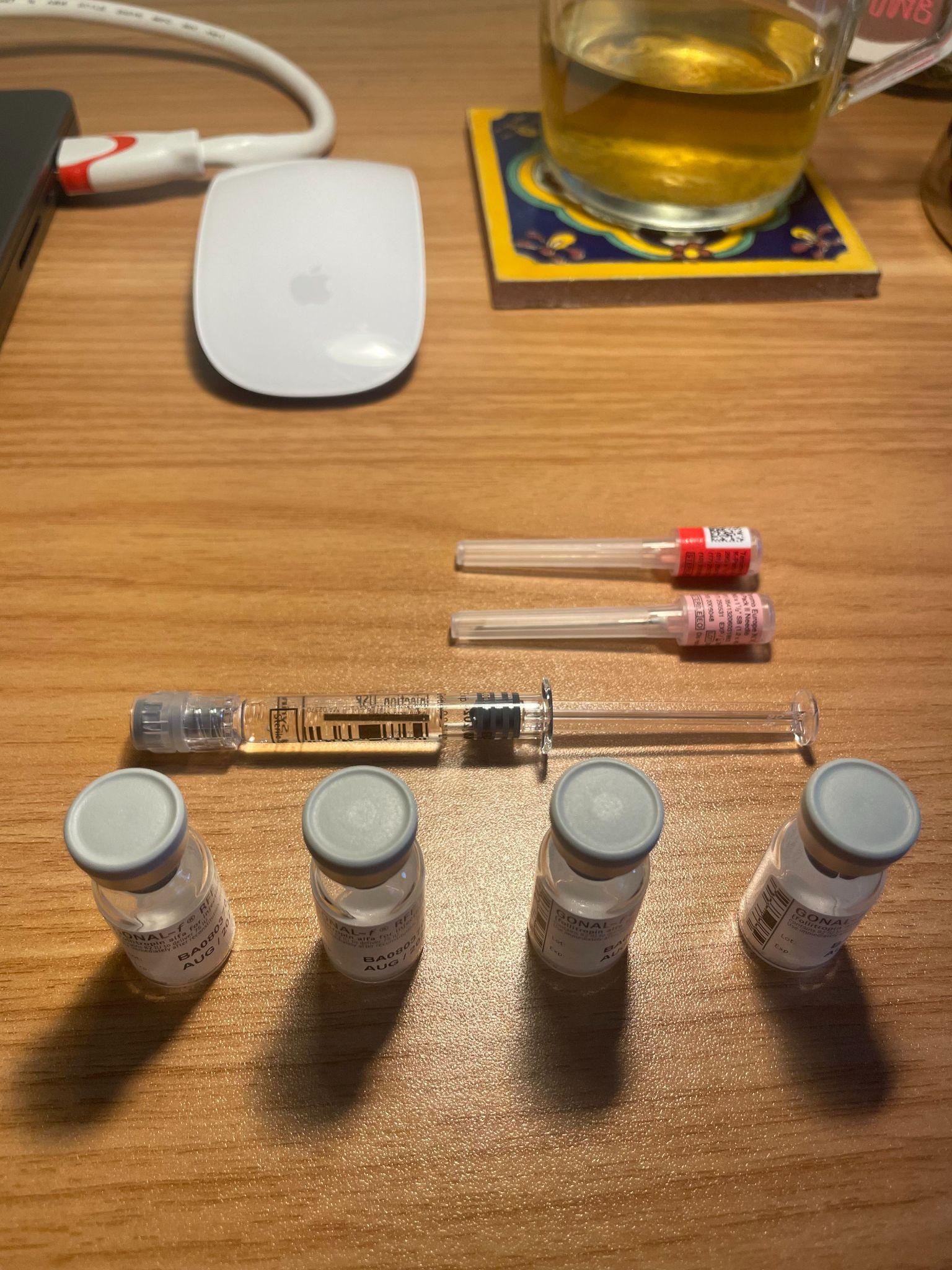 Fertility medication supplies including Gonal-f vials, syringes, and needle tips on a wooden table.