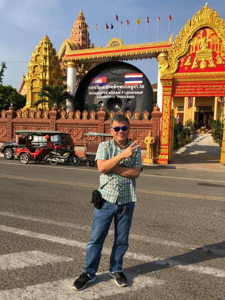 Sam posing with a peace sign in front of the ornate golden friendship gate between Cambodia and Thailand
