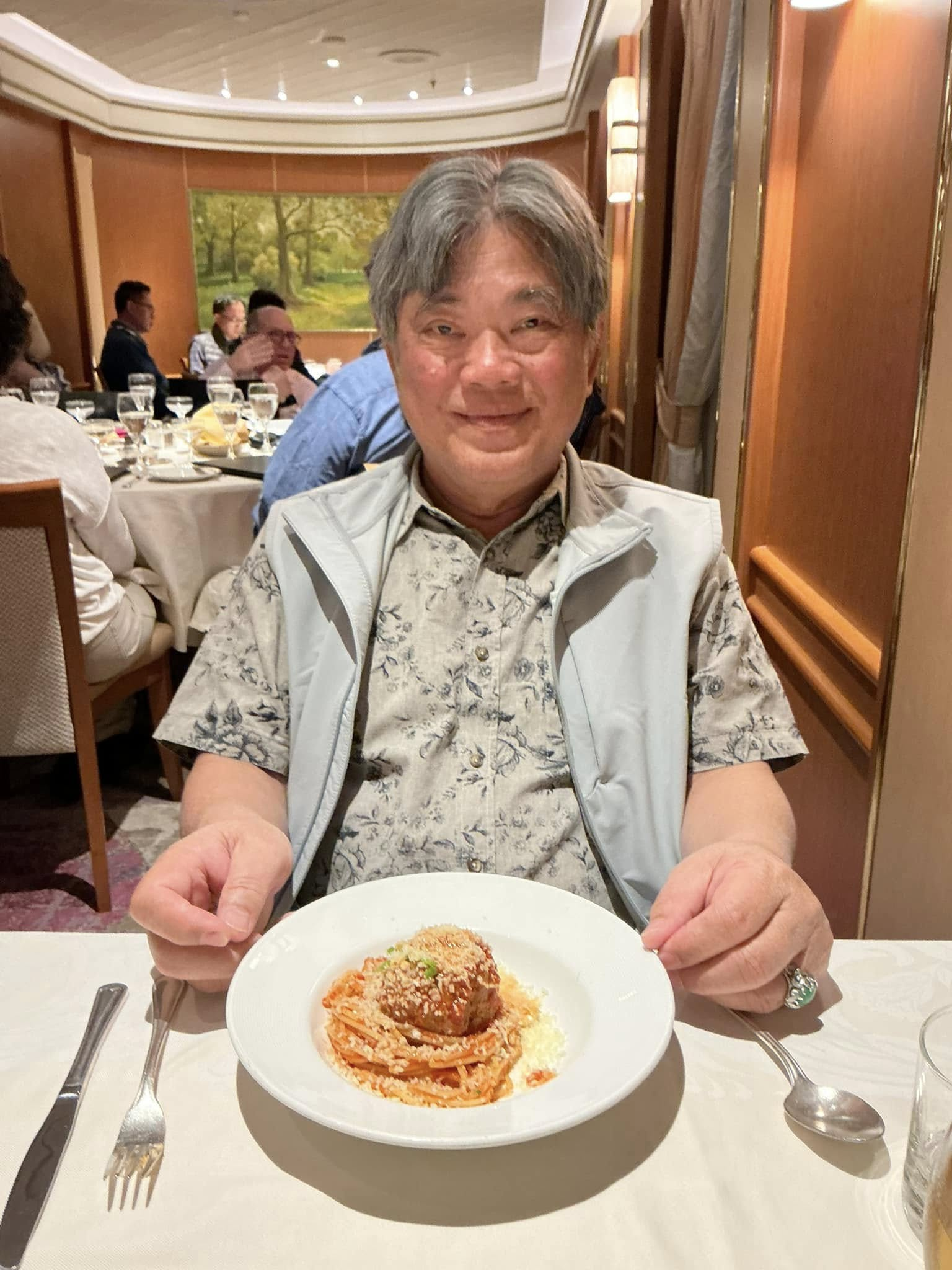 Sam smiling at a restaurant table in front of a plate of pasta and meatballs