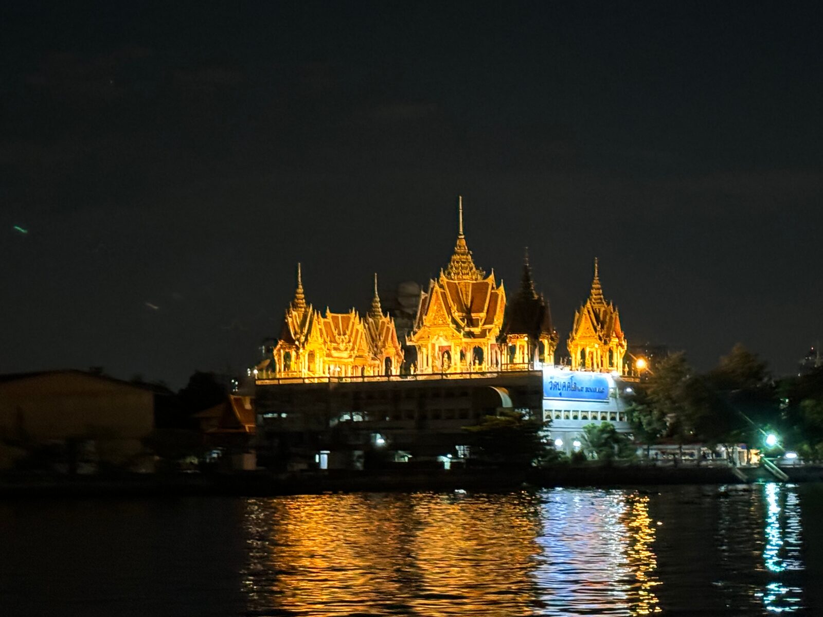 A golden Thai temple lit up at night along the Chao Phraya river